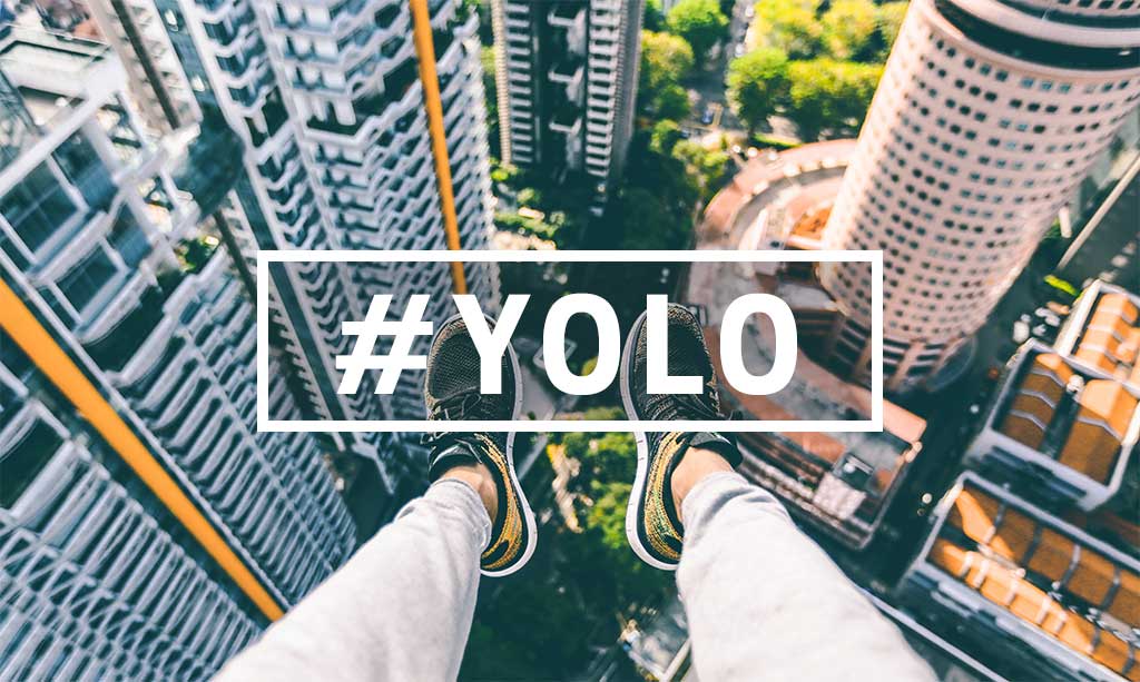 Feet hanging out over city below with text overlay of #YOLO