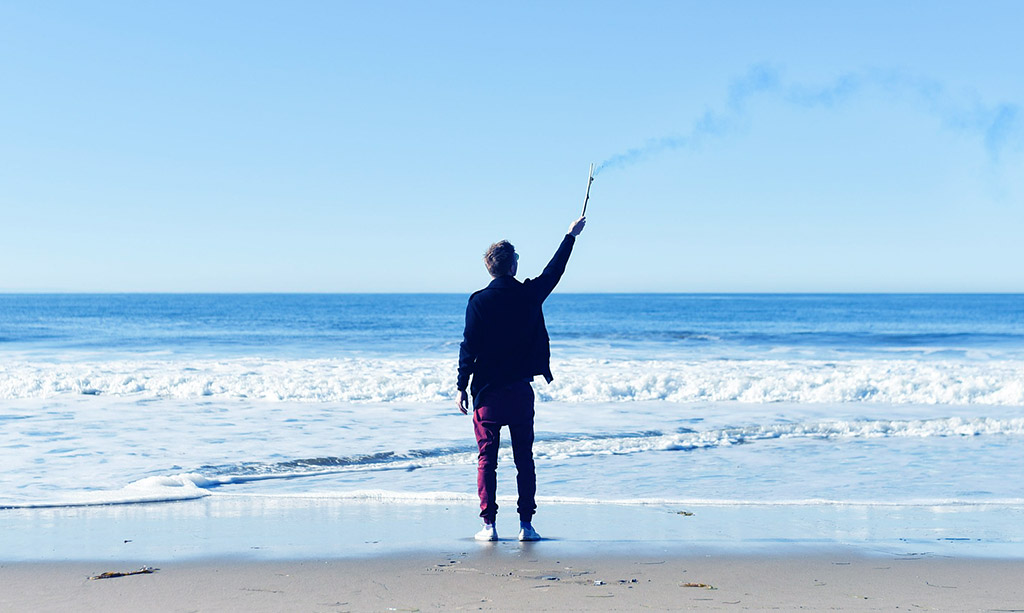 Guy with a flare on the beach contemplating life as a single male.