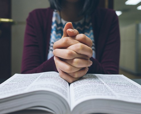 Woman praying in peace with her hands on the bible